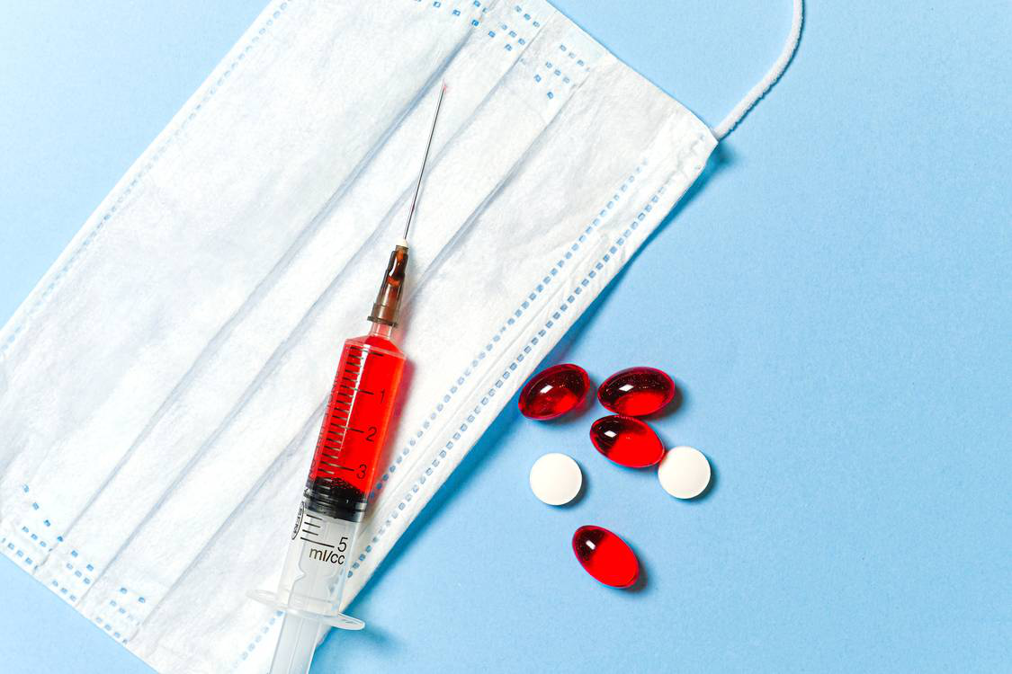 A syringe, facemask, and pills on the table.